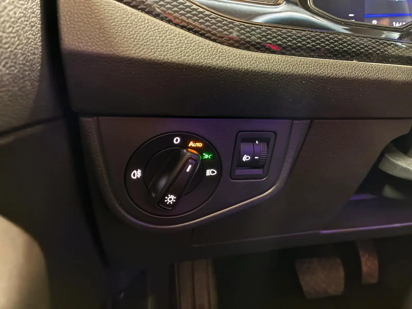 Gros plan sur le bouton de commande des phares avec réglage automatique dans l’habitacle noir de la Volkswagen Polo 2022.
