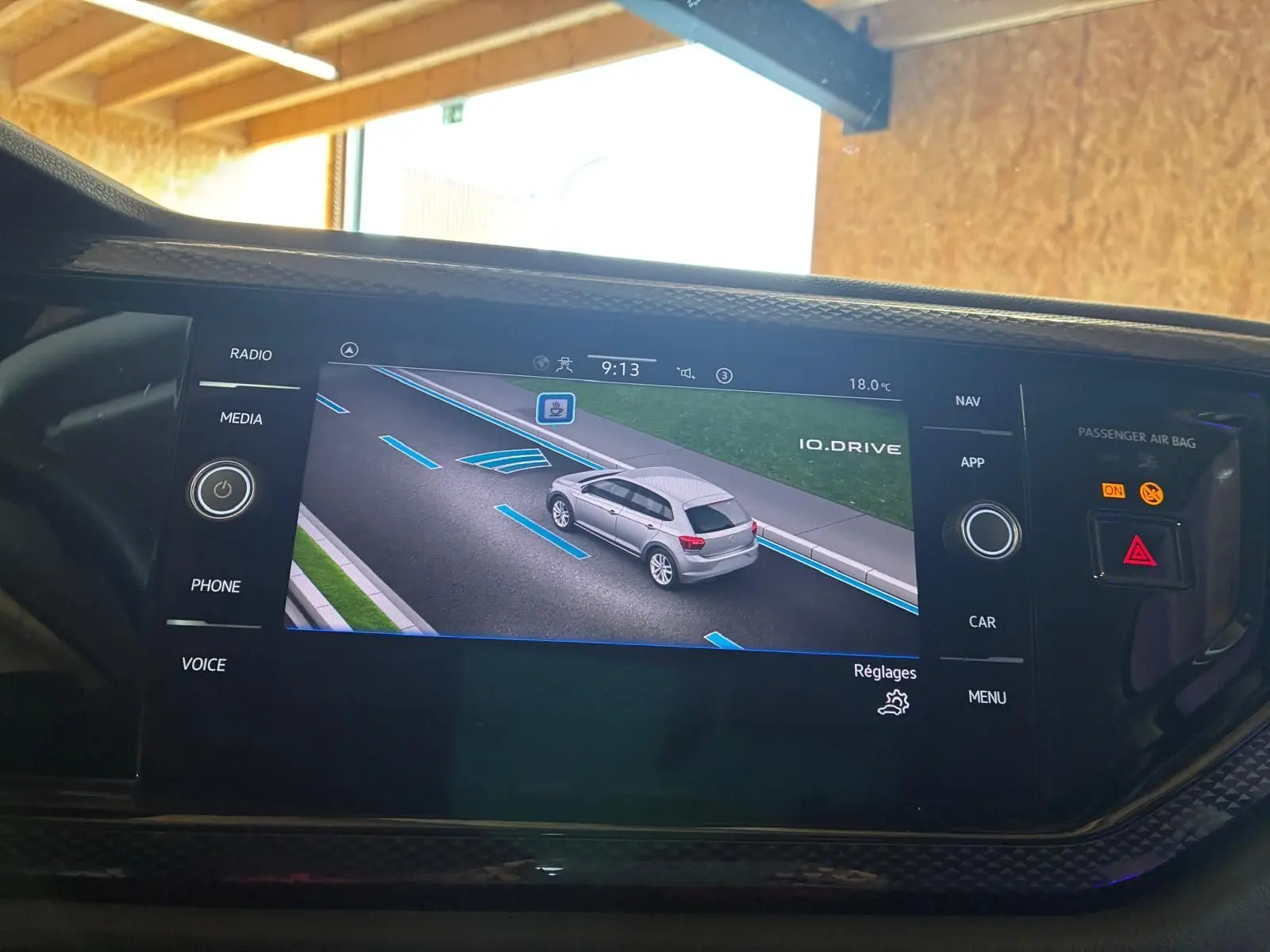 Vue écran intérieur montrant la Polo noire 2022 en 3/4 arrière sur la route avec lignes d'aide au stationnement.