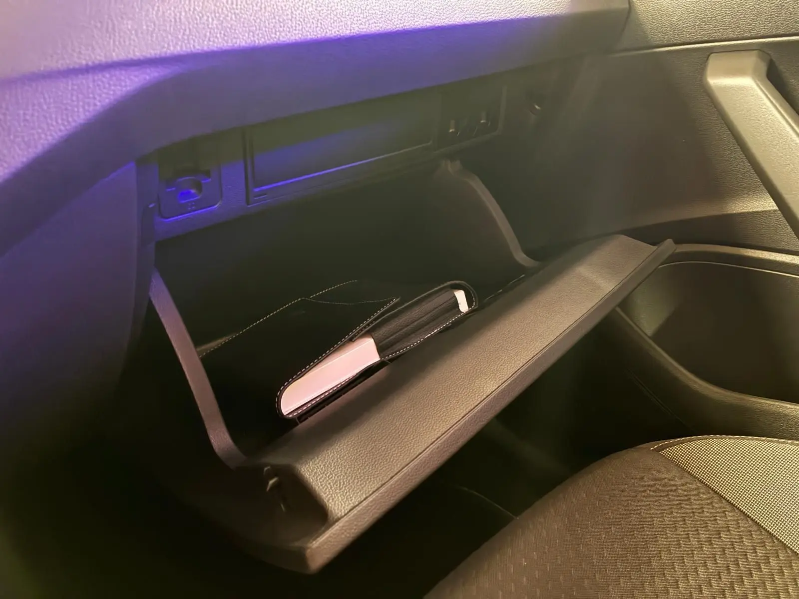 Vue intérieure du coffre à gants ouvert d'une Volkswagen Polo noire, montrant un étui noir et blanc à l'intérieur.