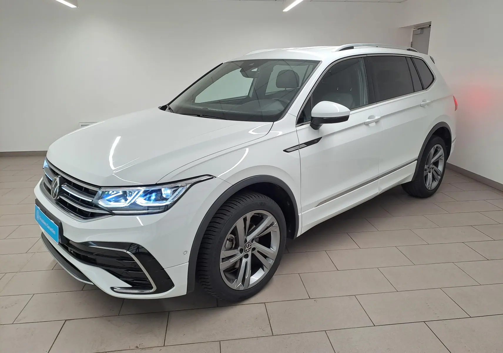 Volkswagen Tiguan Allspace 2.0 TDI 150 DSG7 R-Line blanc pur, vue 3/4 avant droit avec phares allumés.