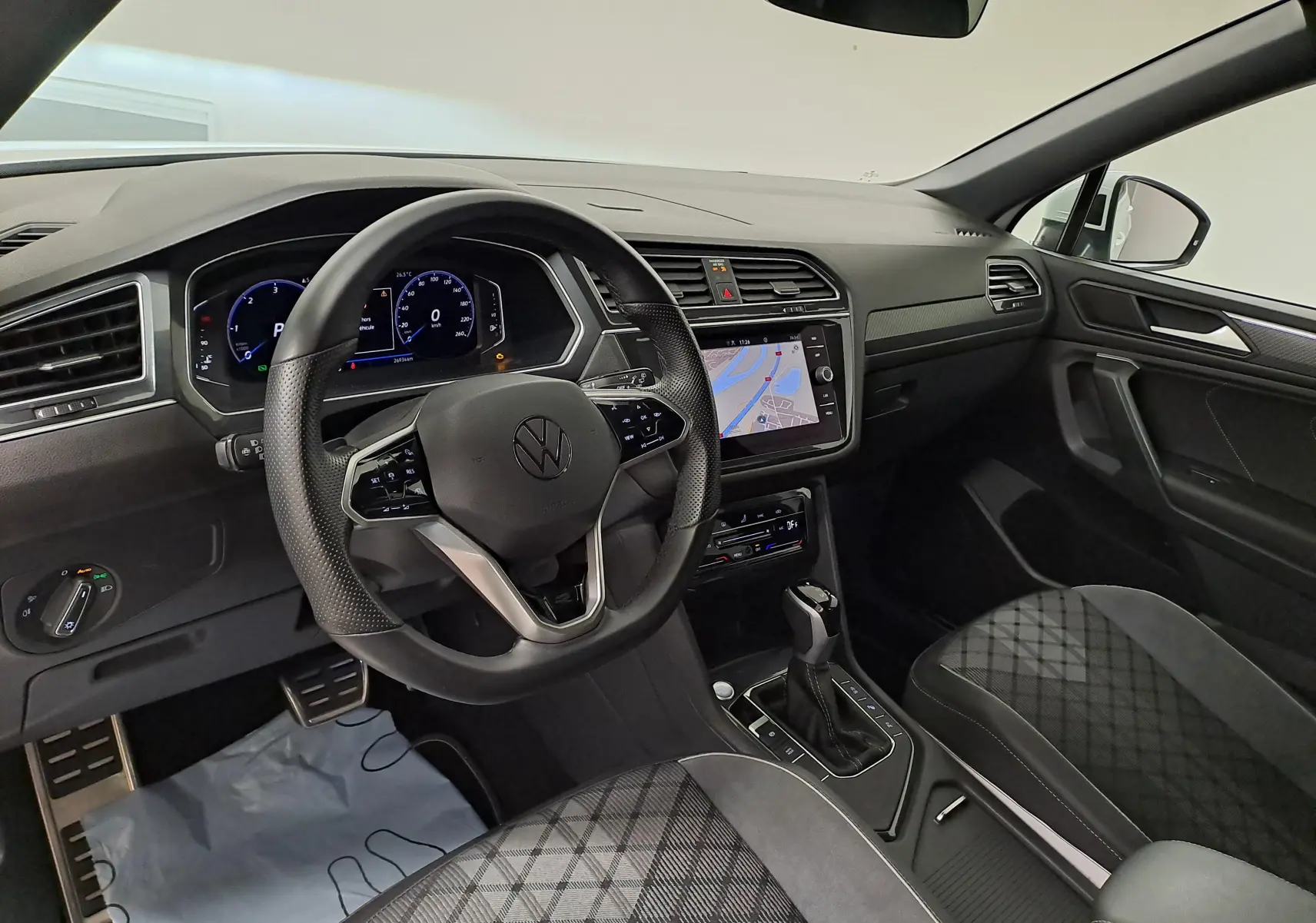Intérieur du Volkswagen Tiguan Allspace R-Line 2023 vu côté conducteur, avec tableau de bord numérique et sellerie noire à motifs.
