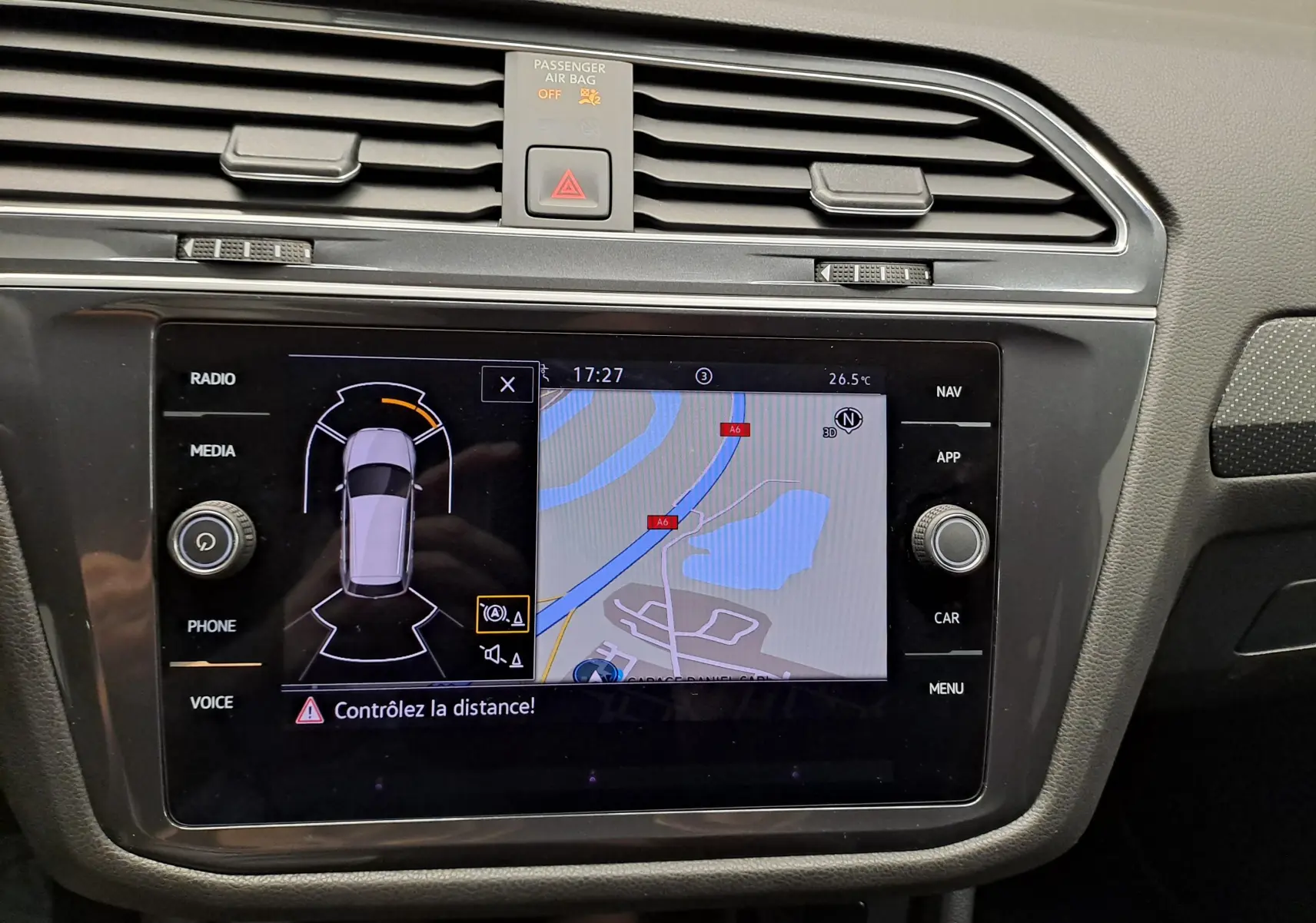 Vue rapprochée de l’écran tactile central du Volkswagen Tiguan Allspace blanc, affichant la navigation et l’aide au stationnement.