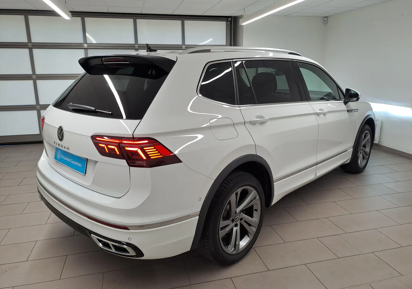 Vue 3/4 arrière droite du Volkswagen Tiguan Allspace blanc pur 2023 en finition R-Line avec feux LED distinctifs.