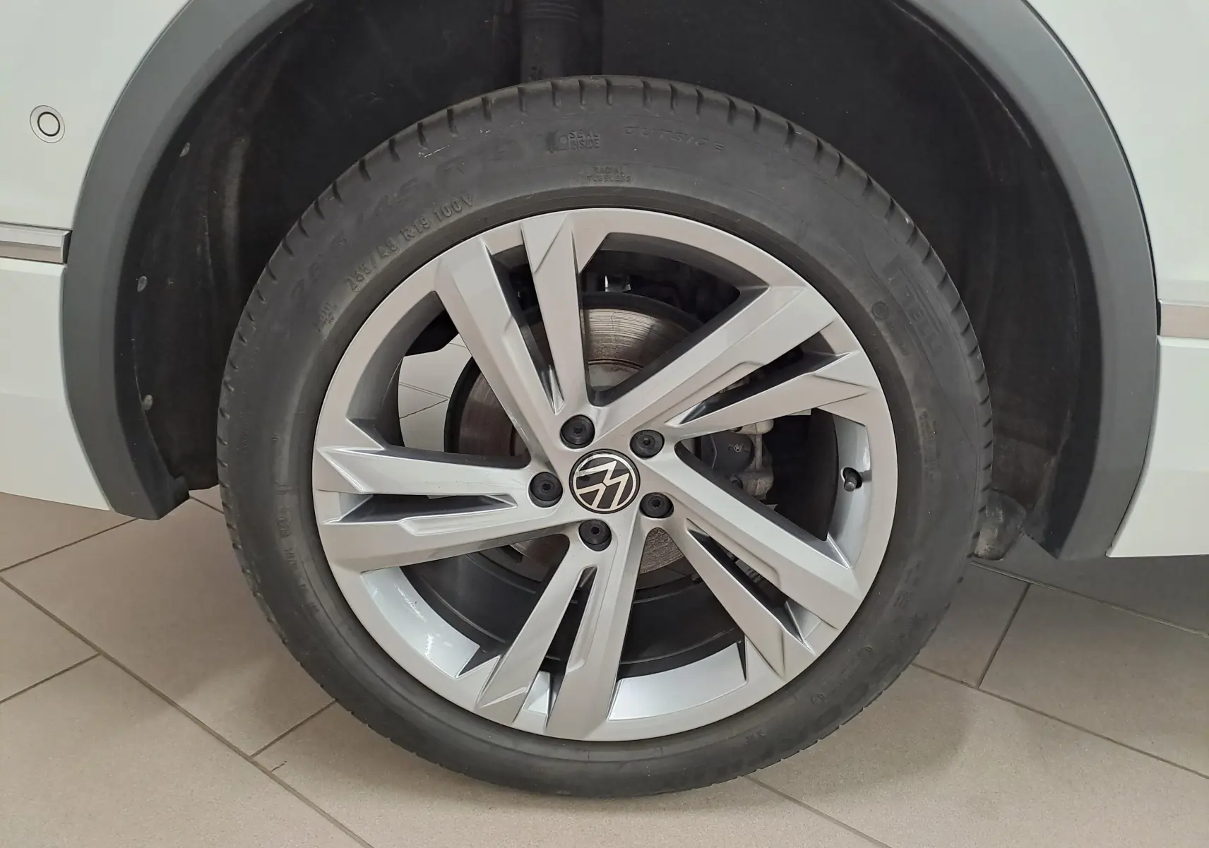 Gros plan sur la roue avant gauche du Volkswagen Tiguan Allspace blanc pur, jante alliage R-Line à design moderne.
