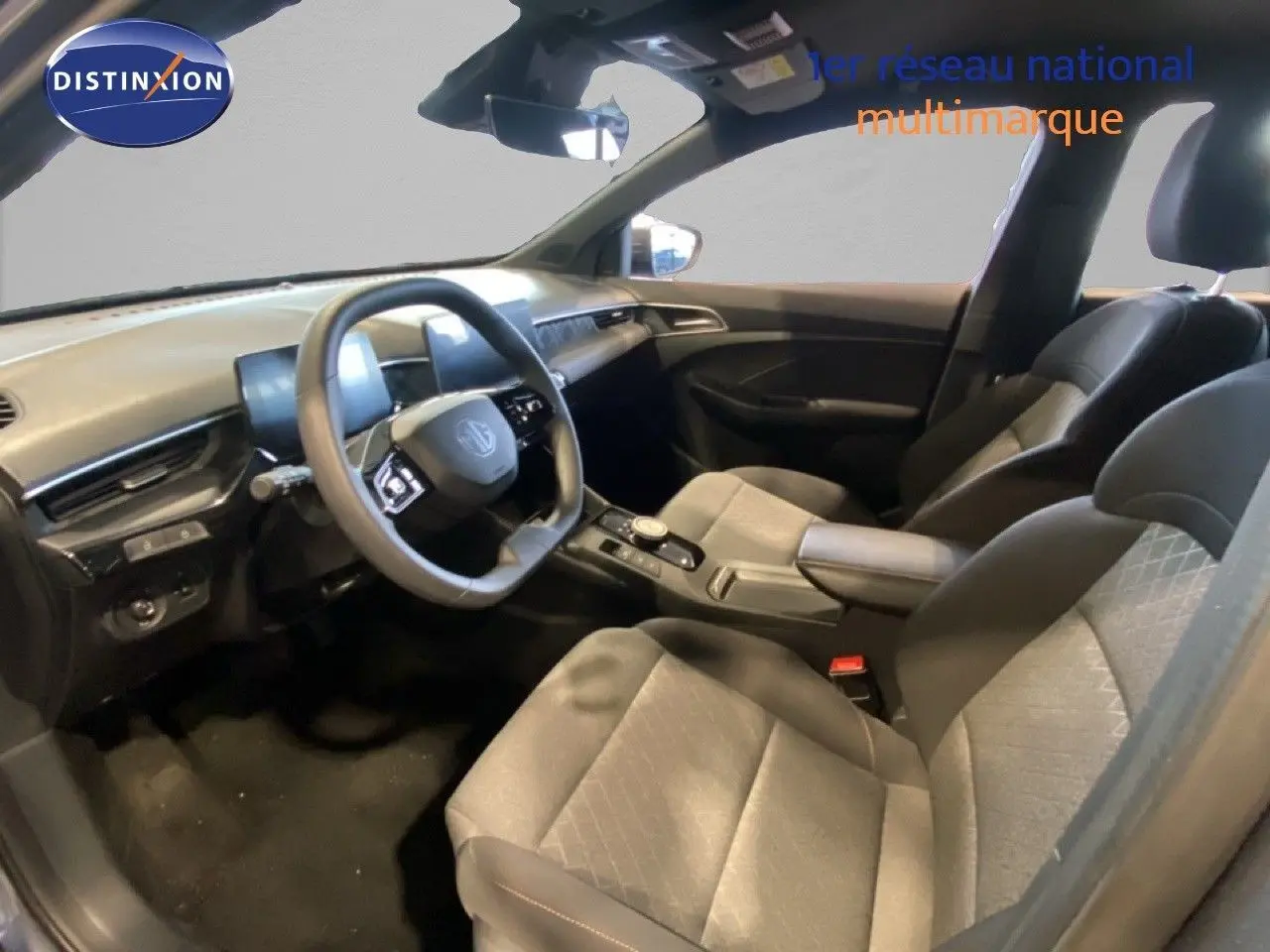 Intérieur de MG3 1.5 Hybrid 2024 vu côté conducteur, sièges tissu gris et tableau de bord moderne noir.