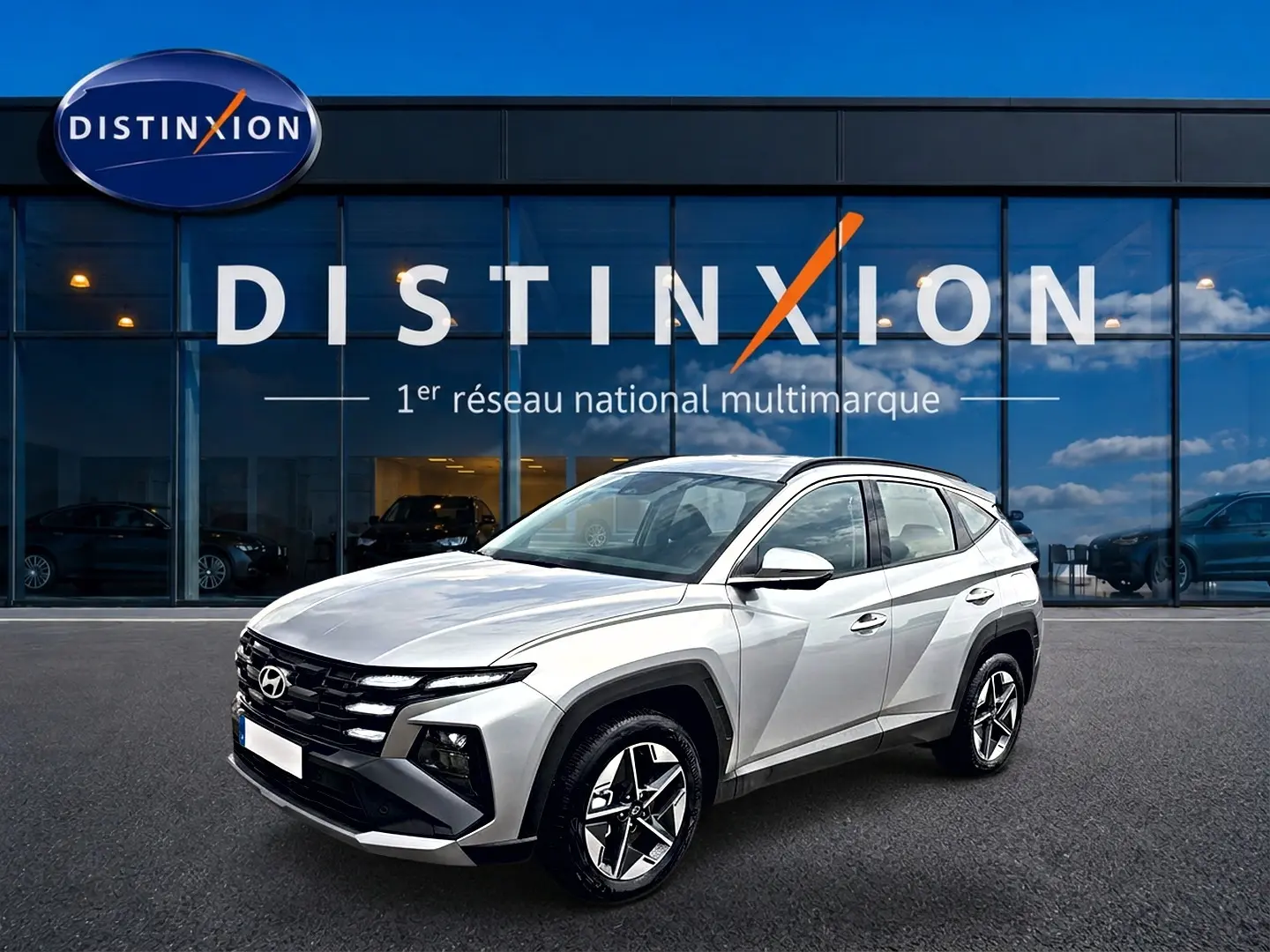 Hyundai Tucson gris shimmering en 3/4 avant droit devant une vitrine Distinxion, jantes alu et lignes anguleuses visibles.