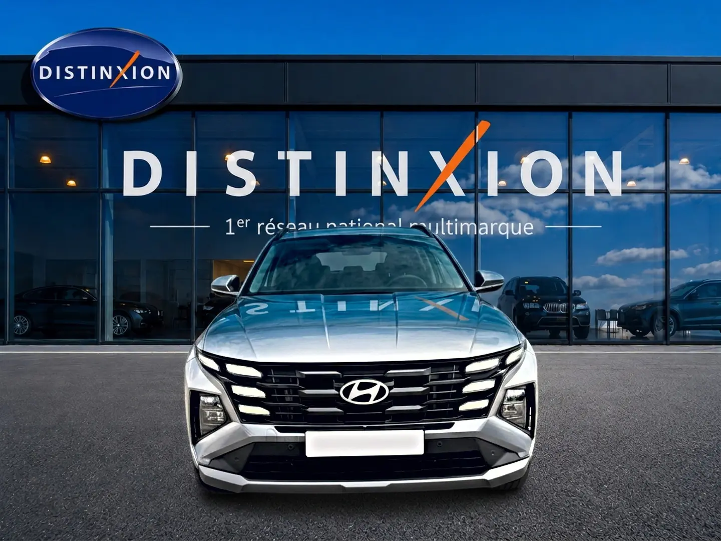 Vue frontale d'un Hyundai Tucson gris shimmering 2026 avec calandre noire distinctive, stationné devant un showroom Distinxion.