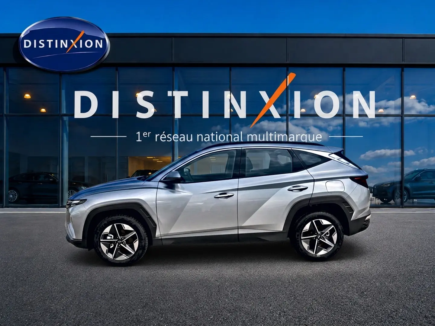 Hyundai Tucson gris shimmering en profil droit devant une vitrine avec logo Distinxion visible en arrière-plan.