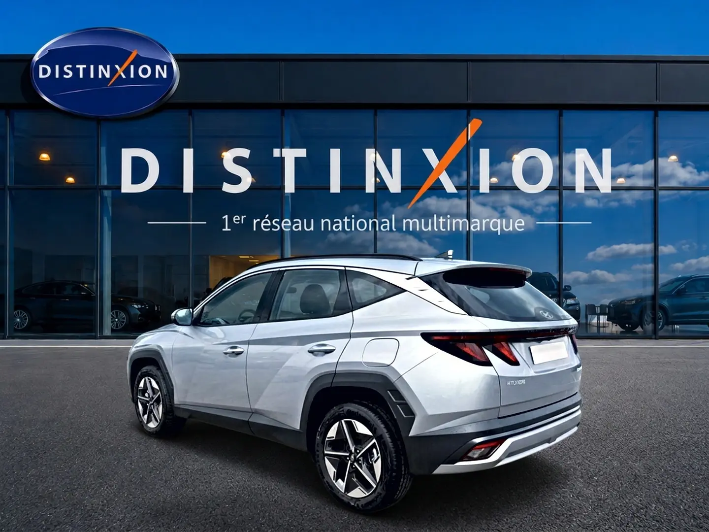 Vue 3/4 arrière droite du Hyundai Tucson gris shimmering devant une vitrine avec logo Distinxion.