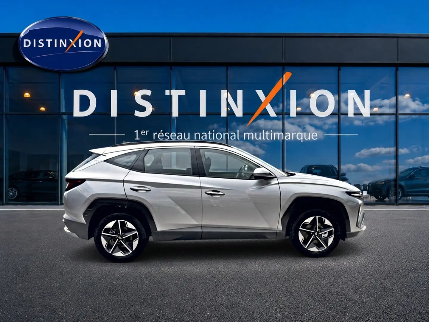 Profil côté gauche du Hyundai Tucson 2026 gris shimmering devant une vitrine avec logo Distinxion.