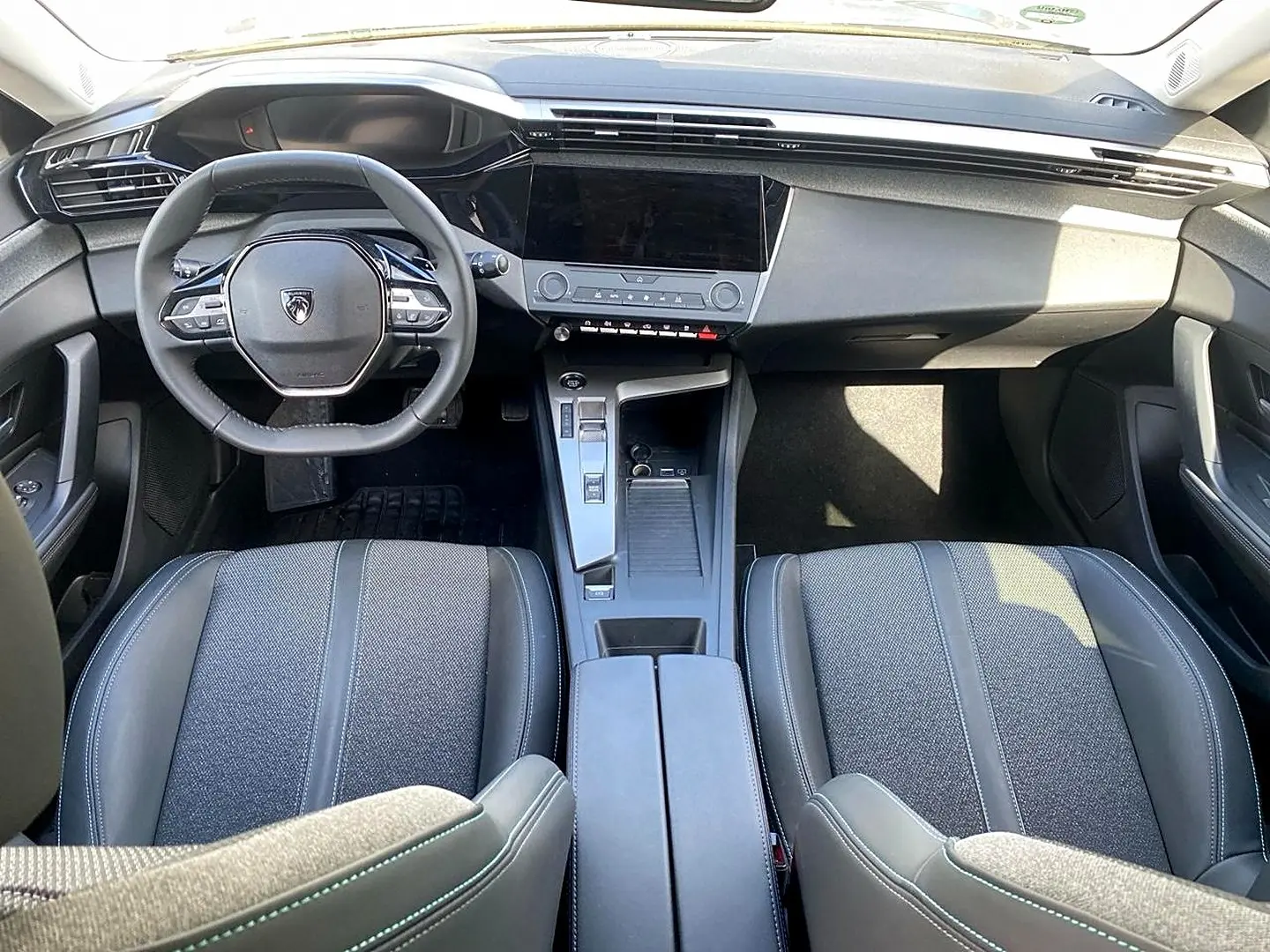 Intérieur de la Peugeot 308 2025 vu de face, montrant le tableau de bord noir et les sièges gris avec surpiqûres.