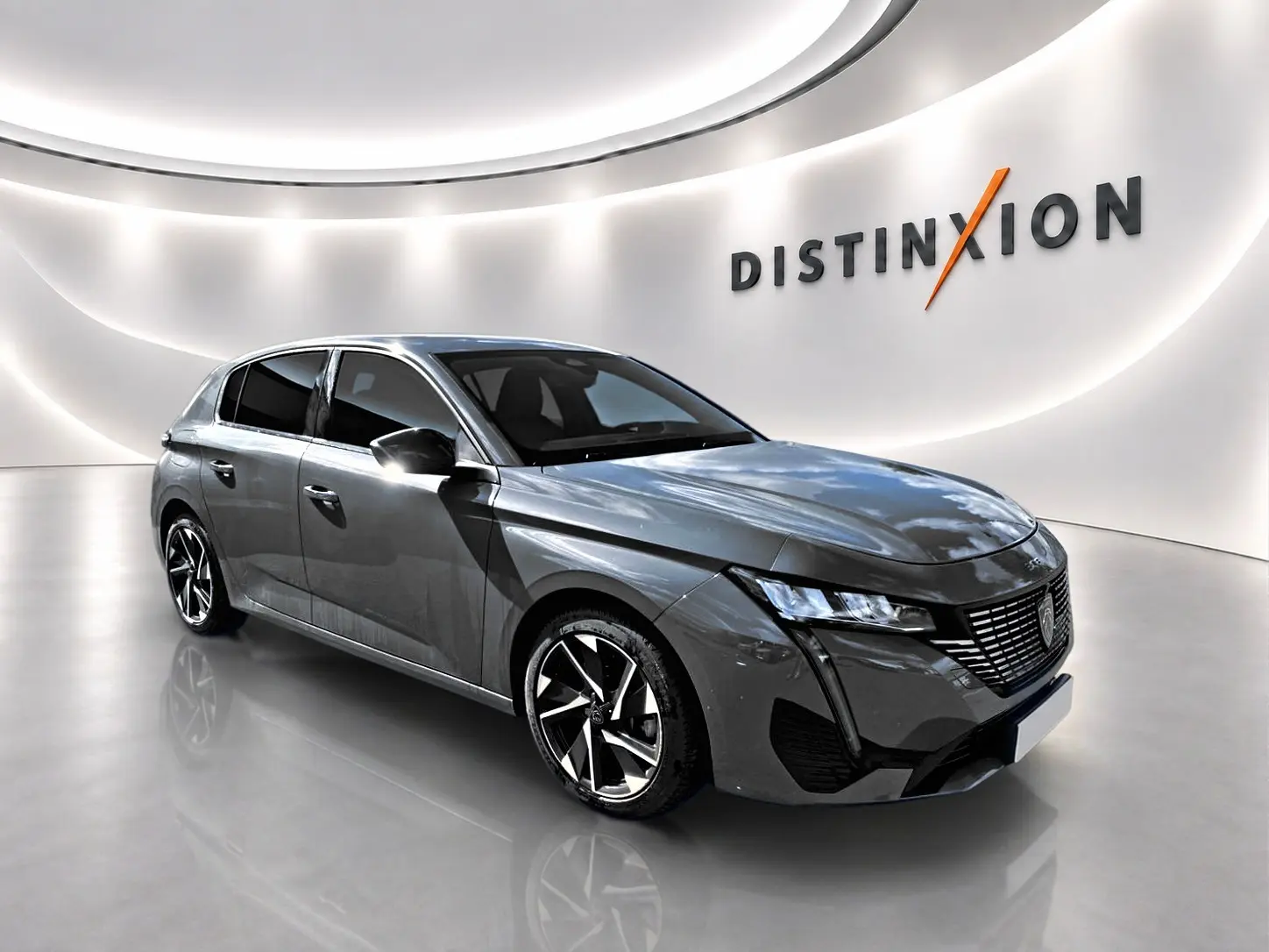 Peugeot 308 gris en 3/4 avant droit dans un showroom lumineux avec jantes alliage et calandre distinctive.