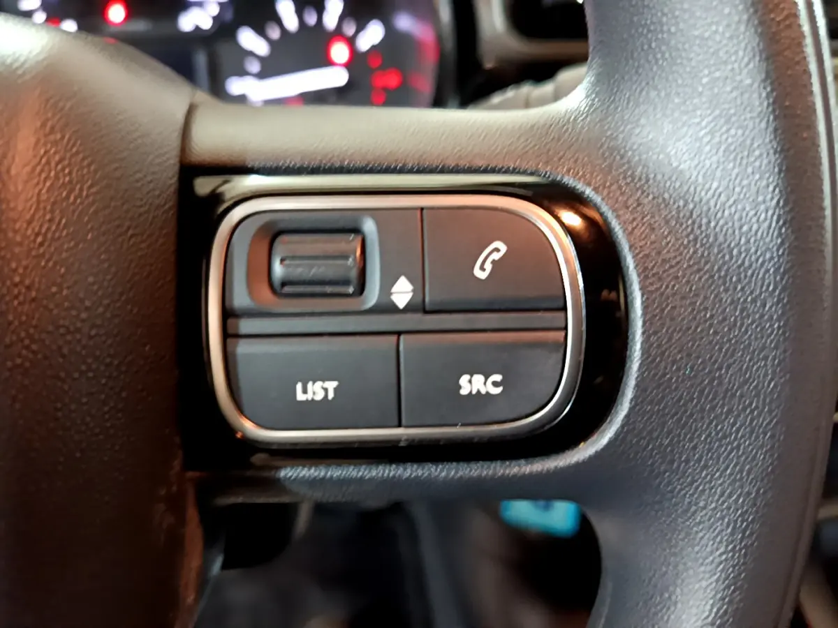 Gros plan sur les commandes multifonctions noires du volant de la Citroën C3 beige, avec tableau de bord flou en arrière-plan.