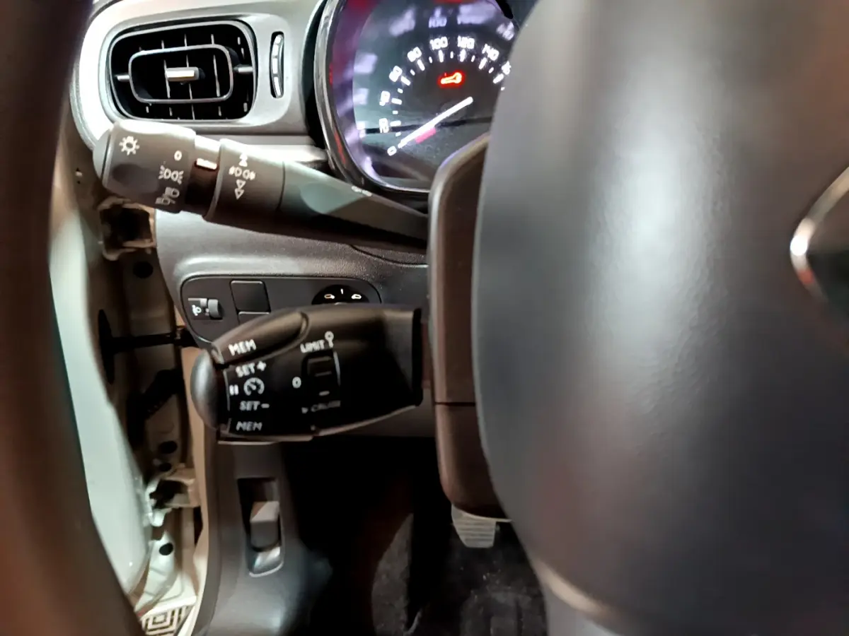 Gros plan sur la colonne de direction et le tableau de bord de la Citroën C3 beige, avec commandes au volant visibles.