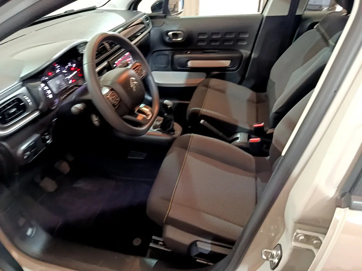 Intérieur de la Citroën C3 beige, vue côté conducteur montrant le tableau de bord et les sièges avant en tissu gris.