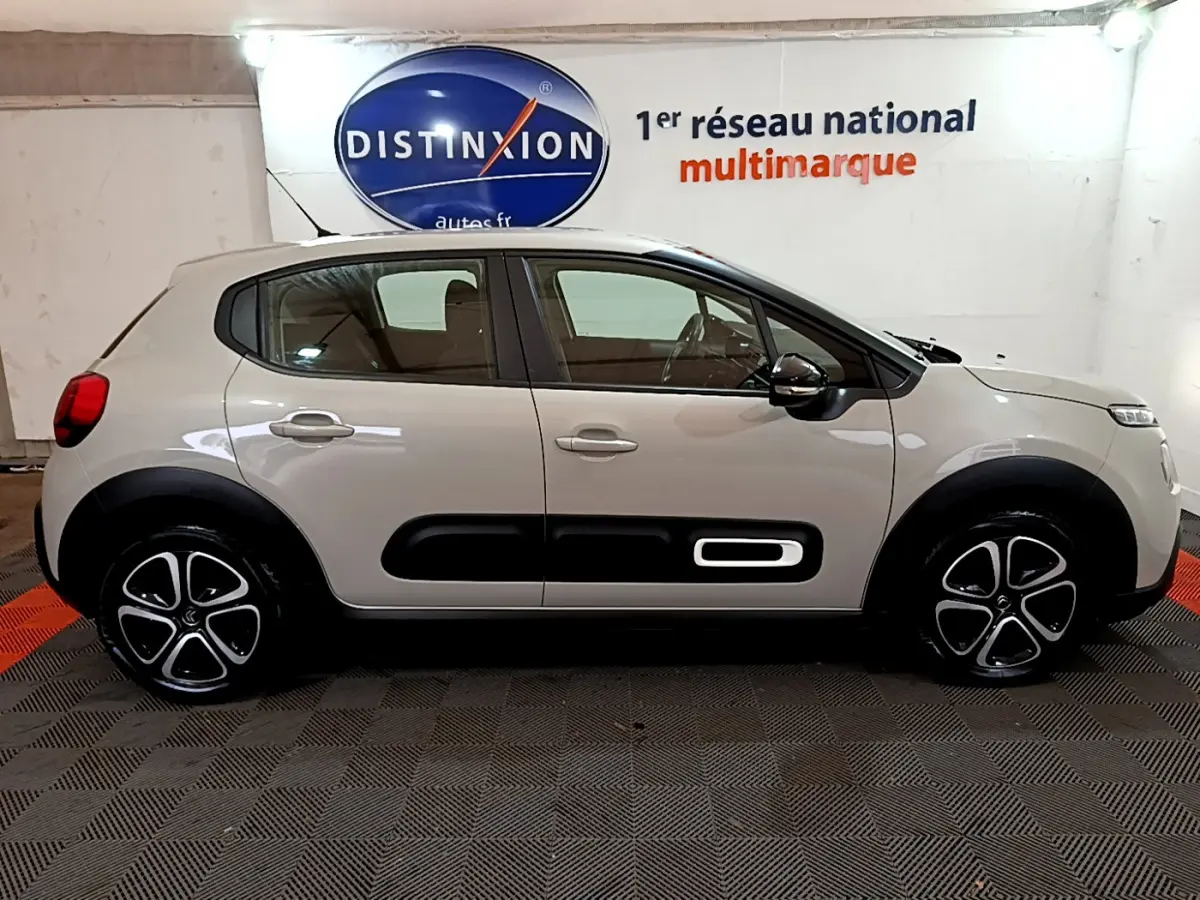 Profil côté gauche d'une Citroën C3 beige 2022 avec protections noires et jantes distinctives en intérieur showroom.