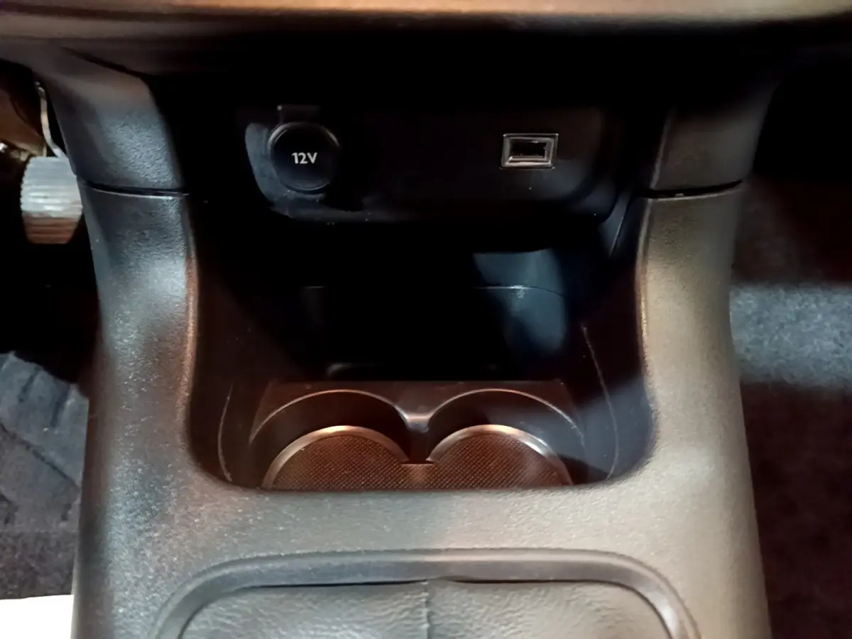 Gros plan sur la console centrale noire de la Citroën C3 beige, montrant prise 12V, port USB et porte-gobelets.