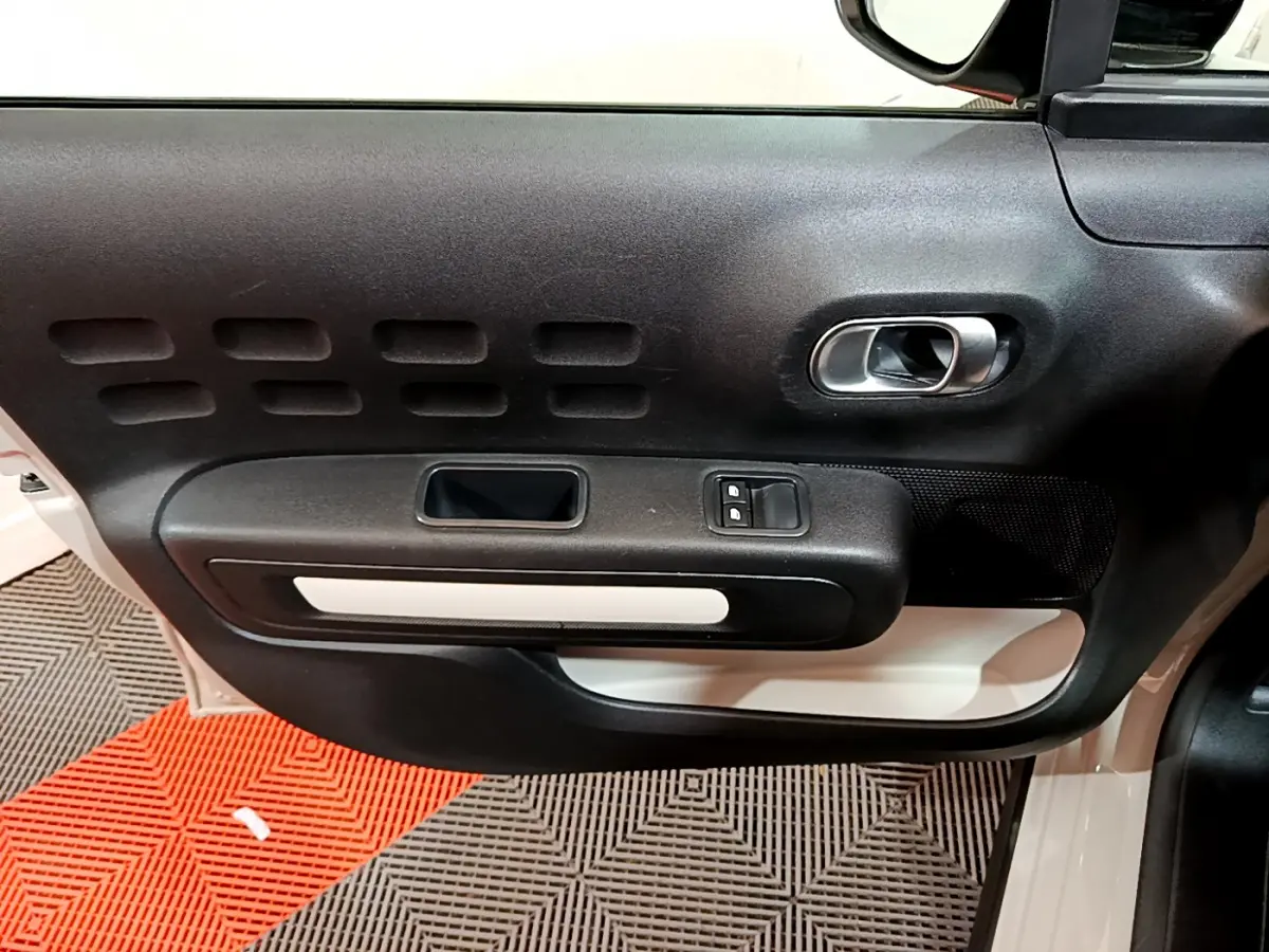 Intérieur de la porte côté conducteur d'une Citroën C3 beige 2022, avec poignée argentée et commandes de vitres.