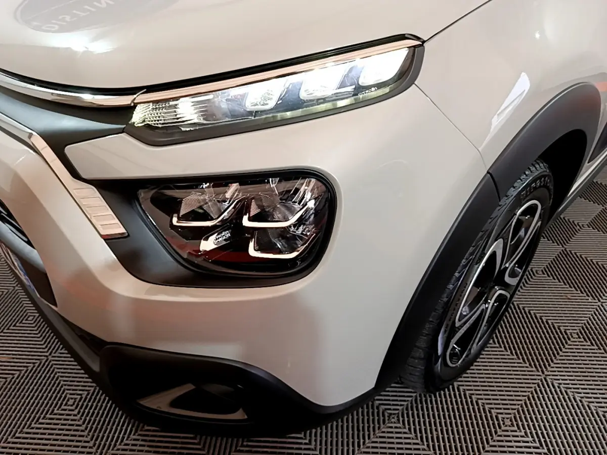 Gros plan sur l'avant droit beige d'une Citroën C3 2022, mettant en valeur ses phares LED et jante noire stylisée.