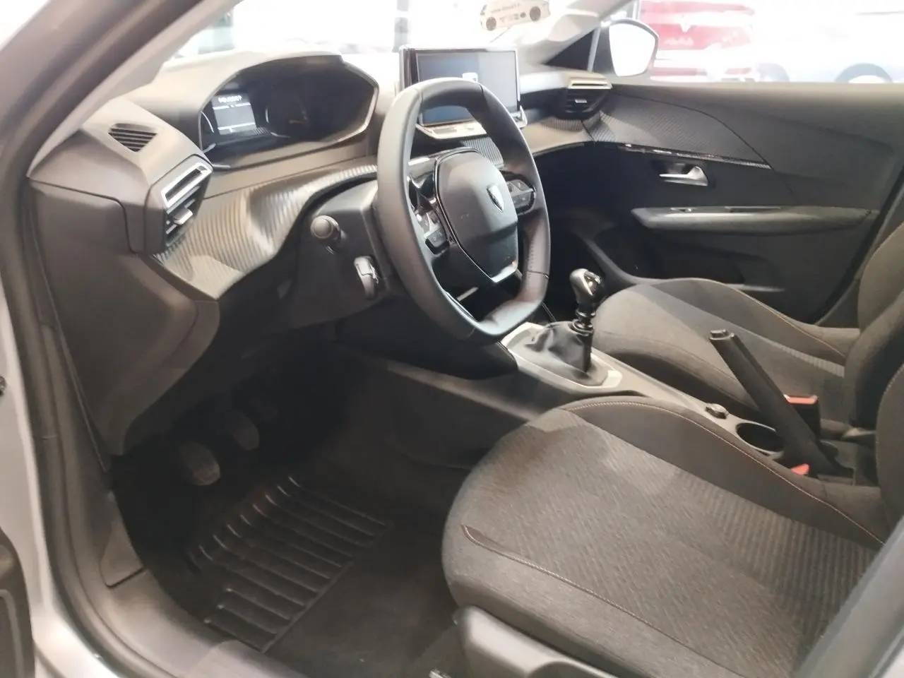 Intérieur avant droit de la Peugeot 208 2025 gris clair, volant cuir, boîte manuelle et tableau de bord moderne.