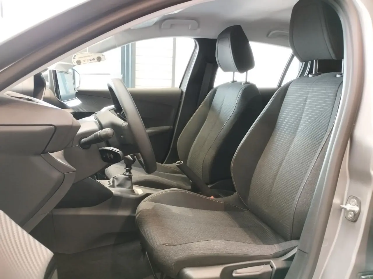 Vue intérieure côté gauche de la Peugeot 208 gris clair, montrant sièges avant en tissu et volant avec boîte manuelle.