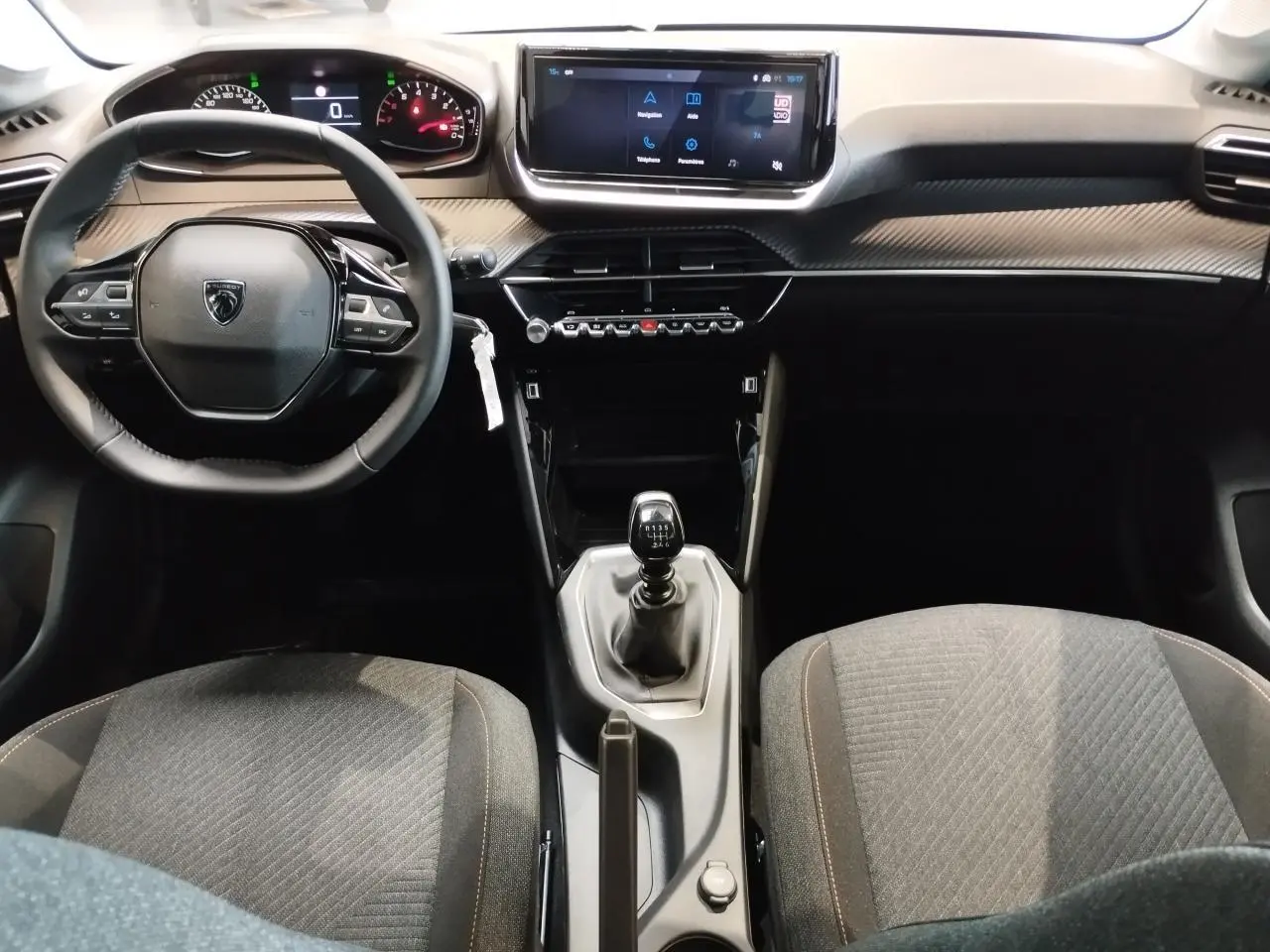 Vue intérieure avant de la Peugeot 208 2025 avec volant compact, écran tactile 10 pouces et levier de vitesse manuel.