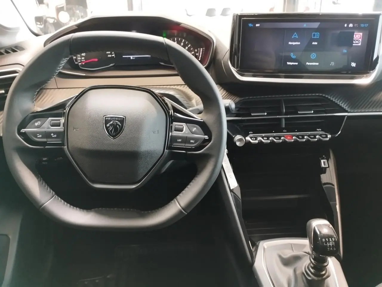 Vue intérieure centrée sur le volant cuir et la console avec écran tactile 10'' de la Peugeot 208 1.2i 12V gris clair, boîte manuelle.