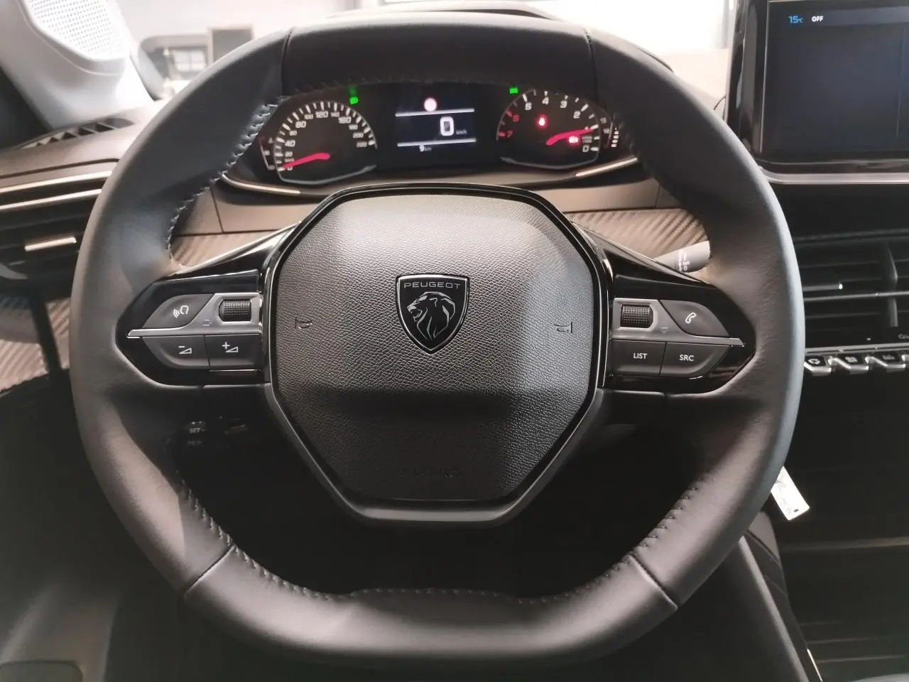 Vue rapprochée du volant noir cuir de la Peugeot 208 2025 avec commandes multimédia et combiné digital en arrière-plan.