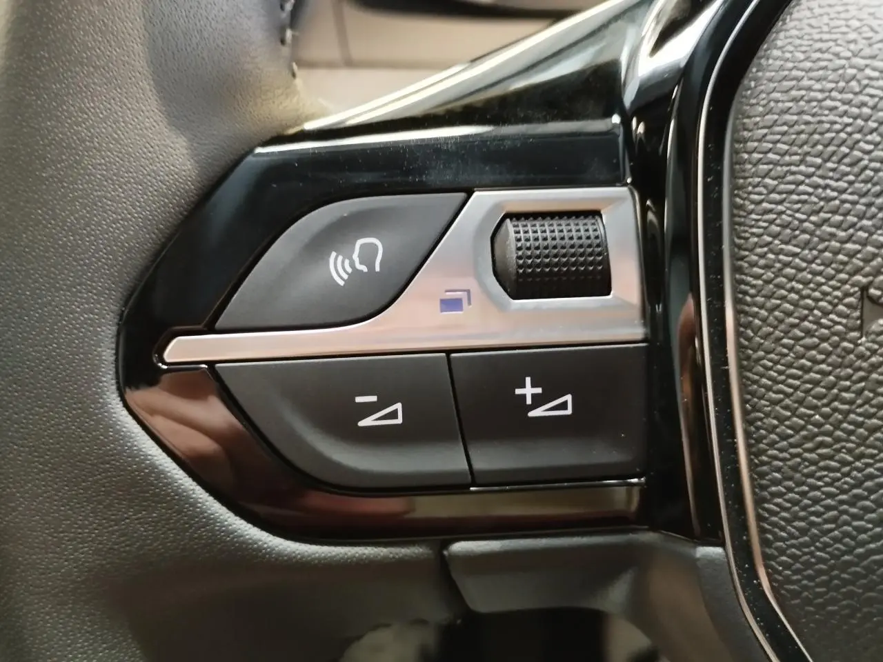 Gros plan sur les commandes noires et argentées du volant de la Peugeot 208 gris clair, version 2025.