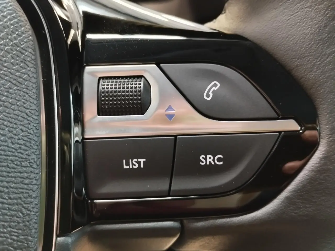 Gros plan sur les commandes multimédia noires et argentées du volant côté gauche d'une Peugeot 208 gris clair.