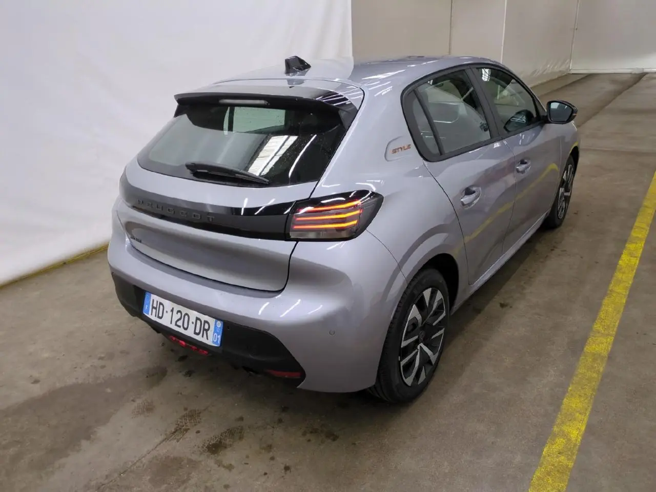 Vue 3/4 arrière droite d'une Peugeot 208 gris clair avec badge Style sur custode et feux arrière à LED 3 griffes.
