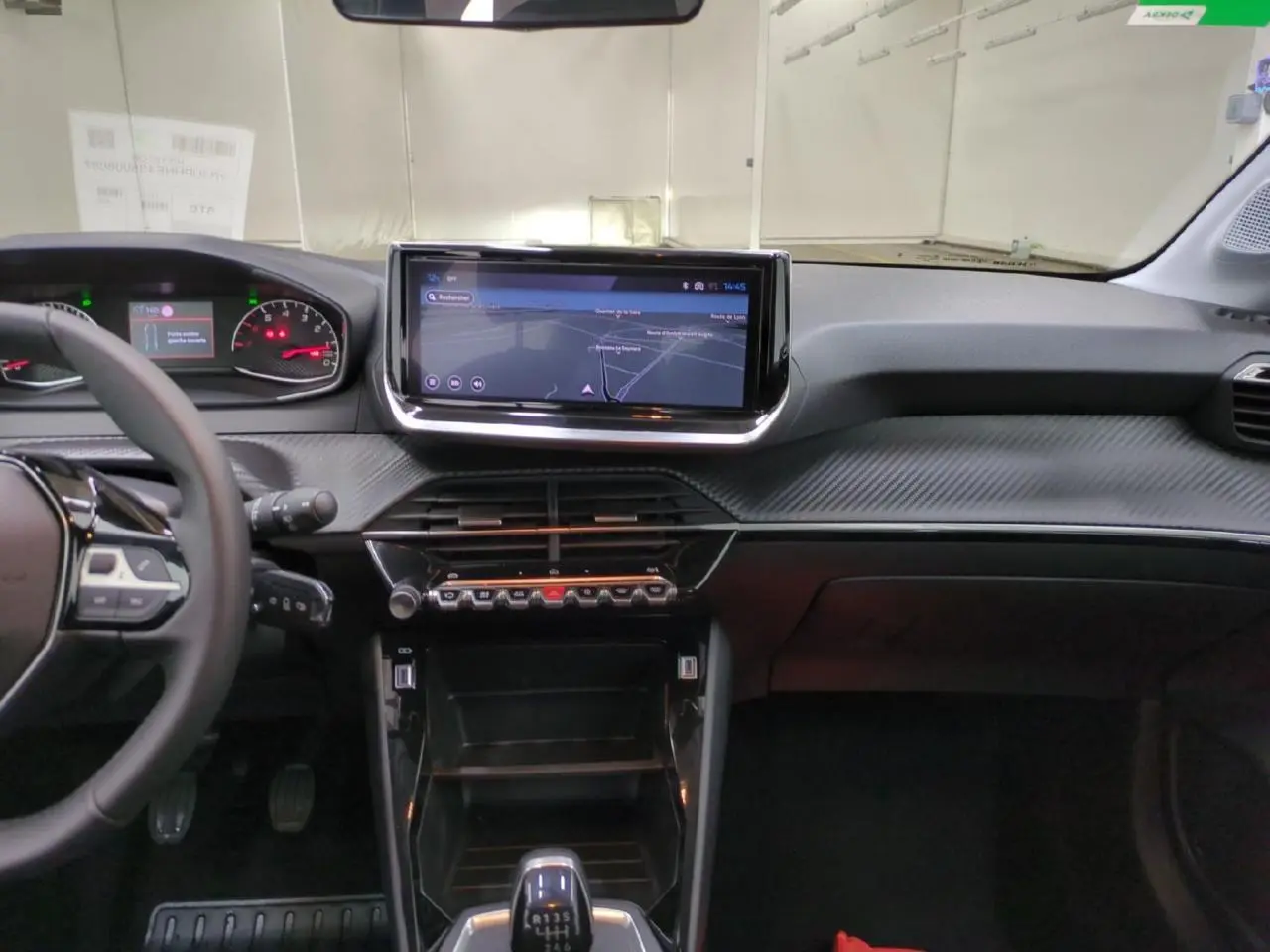 Vue intérieure avant du tableau de bord de la Peugeot 208 2025, avec écran tactile 10 pouces et volant cuir noir.