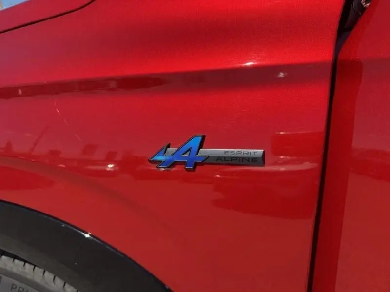 Gros plan sur l’écusson bleu "Esprit Alpine" sur l’aile avant droite d’un Renault Austral rouge flamme 2023.