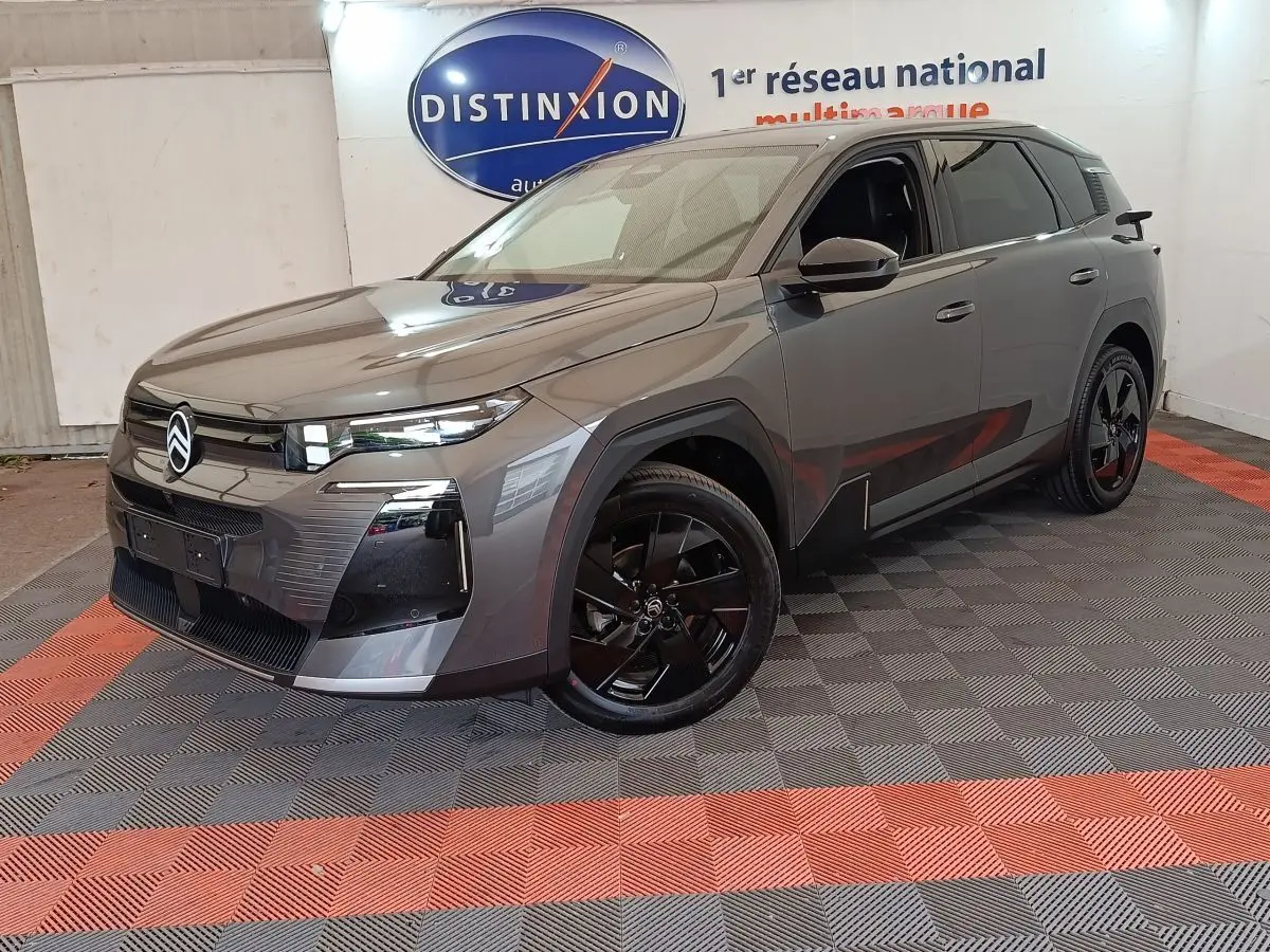 Vue 3/4 avant d'une Citroën C5 hybride gris foncé avec jantes noires et calandre moderne, en intérieur showroom.