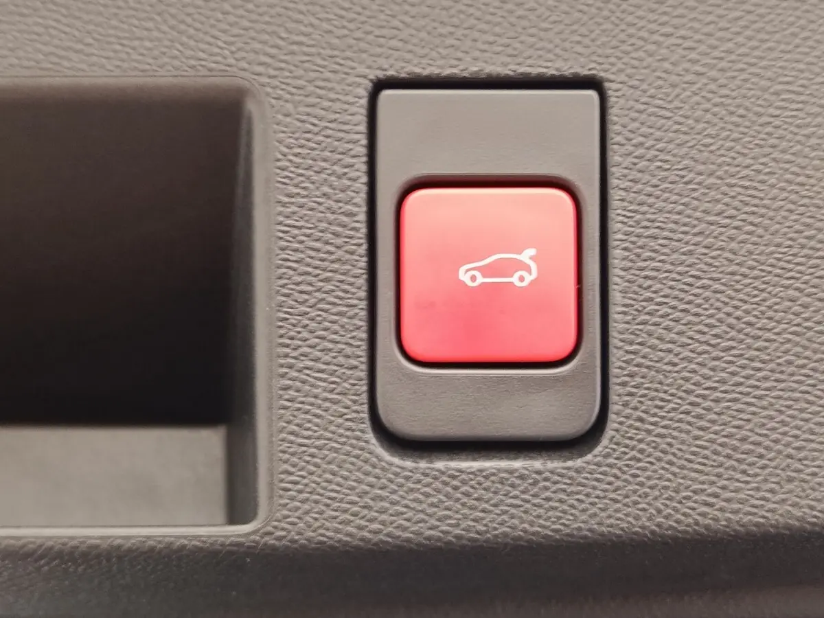 Bouton rouge d'ouverture électrique du coffre sur tableau de bord texturé gris foncé d'une Citroën C5 hybride.