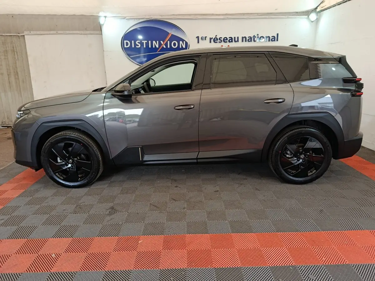 Vue de profil côté gauche d'une Citroën C5 hybride gris foncé avec jantes noires, stationnée en intérieur.