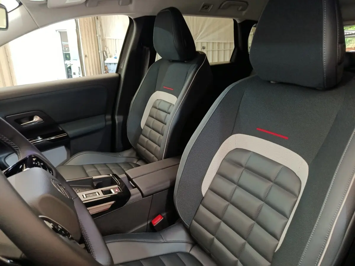 Vue intérieure rapprochée des sièges avant gris foncé avec surpiqûres et détails rouges du Citroën C5 Hybride 2025.
