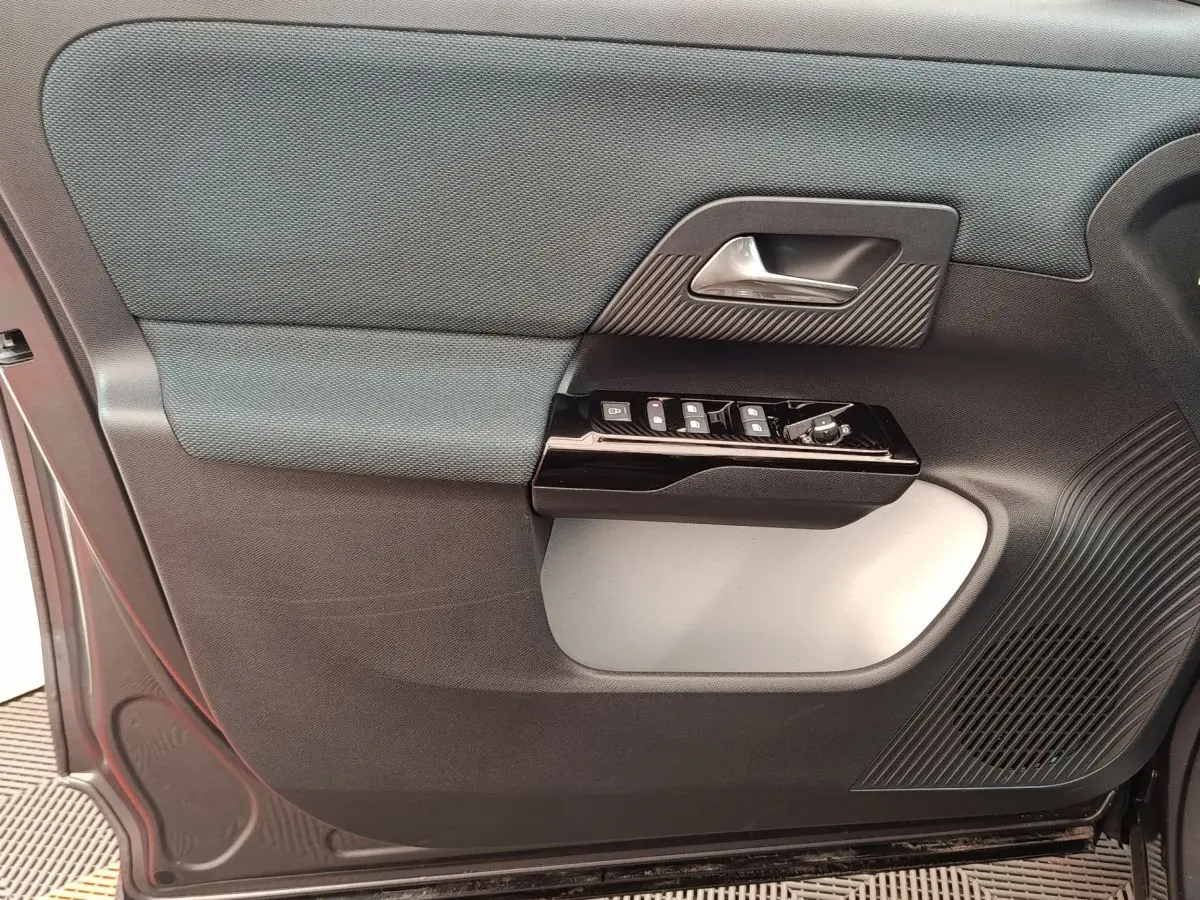 Gros plan sur la porte avant gauche intérieure de la Citroën C5 hybride gris foncé, avec commandes de vitres et poignée argentée.
