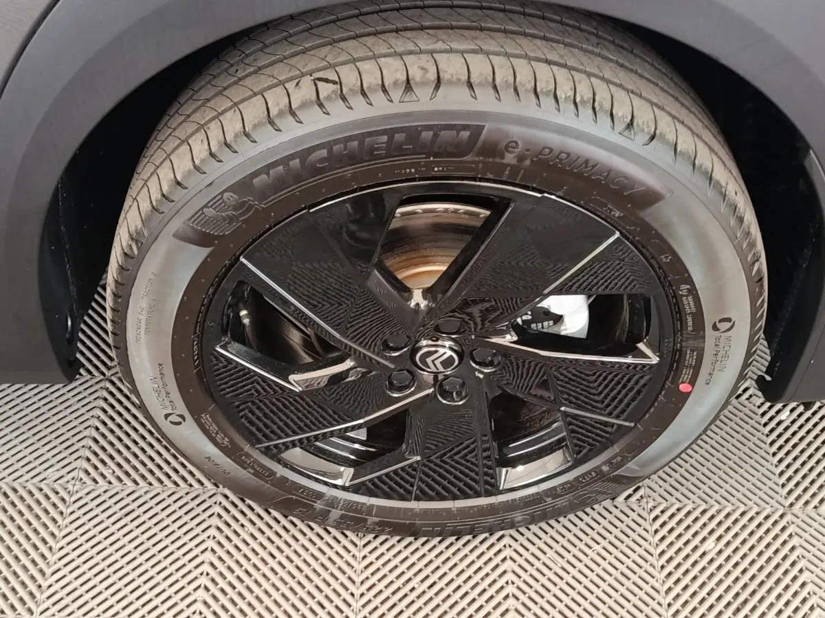Gros plan sur la roue avant droite noire brillante avec logo Citroën sur un Citroën C5 gris foncé.