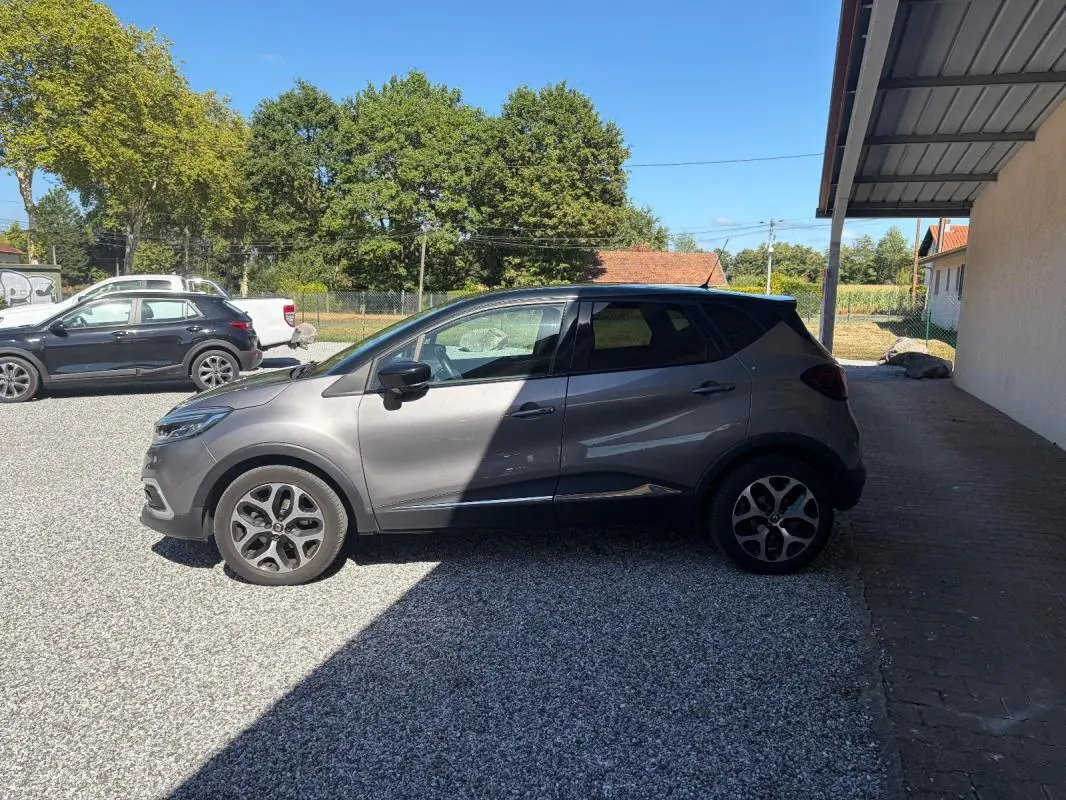 Vue de profil côté gauche d'un Renault Captur gris 2017 avec jantes alliage, stationné sur un sol gravillonné.