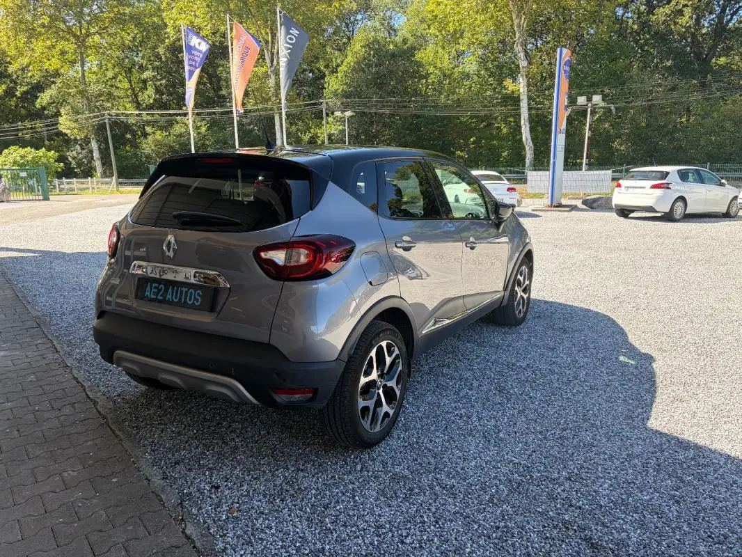 Renault Captur gris 3/4 arrière droit, jantes alliage et toit noir contrasté sur parking ensoleillé.