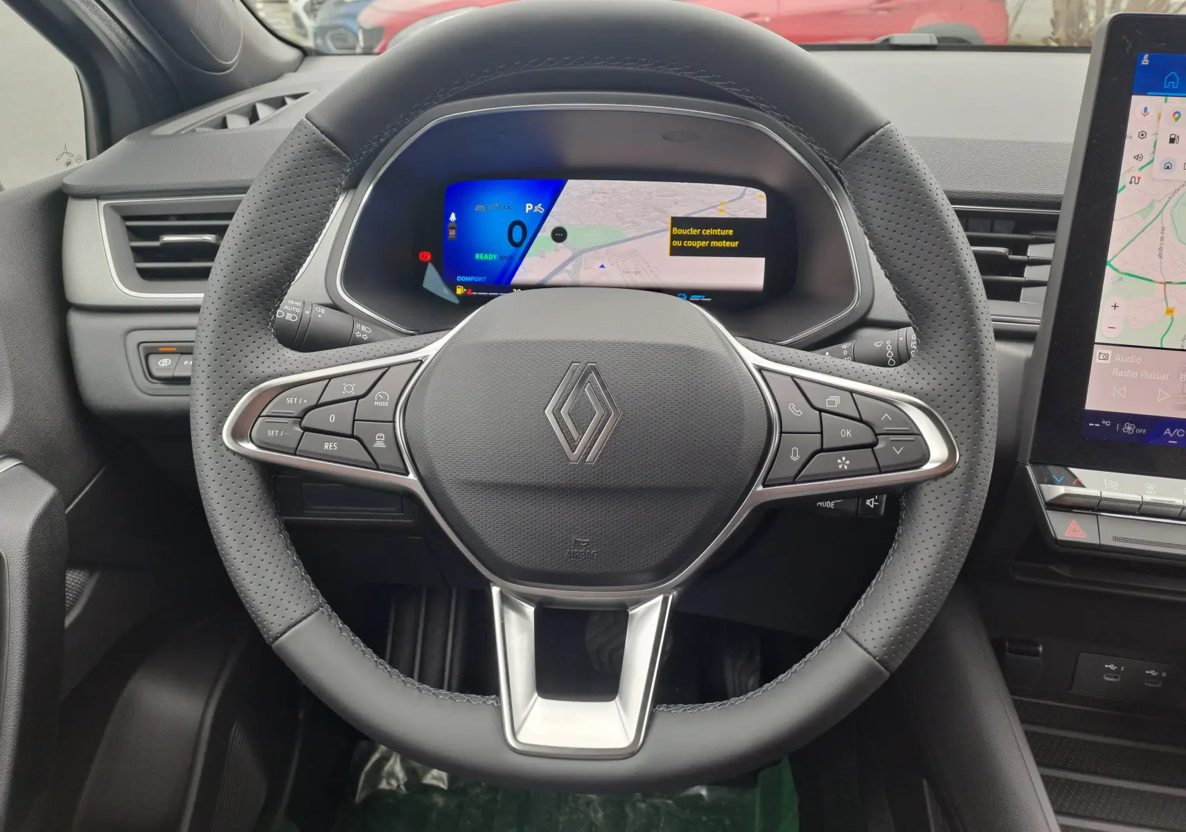 Vue rapprochée du volant en cuir perforé et tableau de bord numérique du Renault Symbioz gris Cassiope 2024.