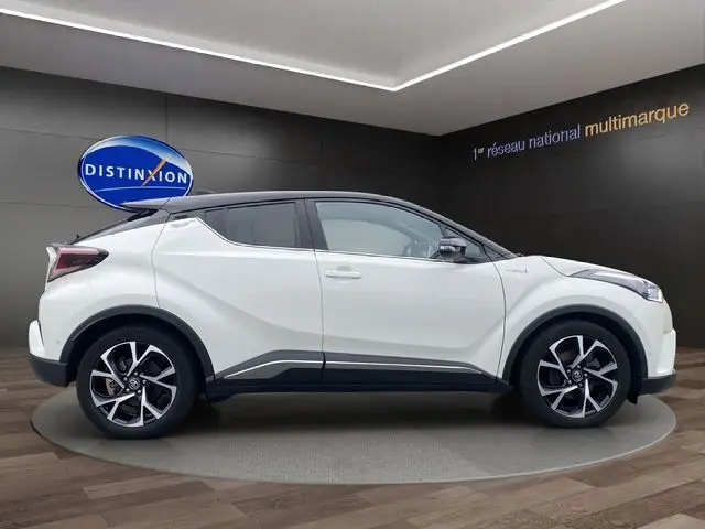 Profil droit d'un Toyota C-HR Hybride blanc avec toit noir, roues alliage et lignes anguleuses marquées.