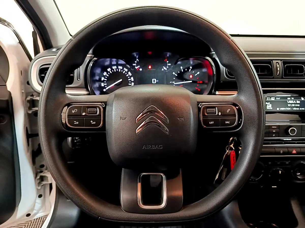 Vue frontale du volant noir de la Citroën C3 blanche 2018 avec commandes multifonctions et tableau de bord éclairé.