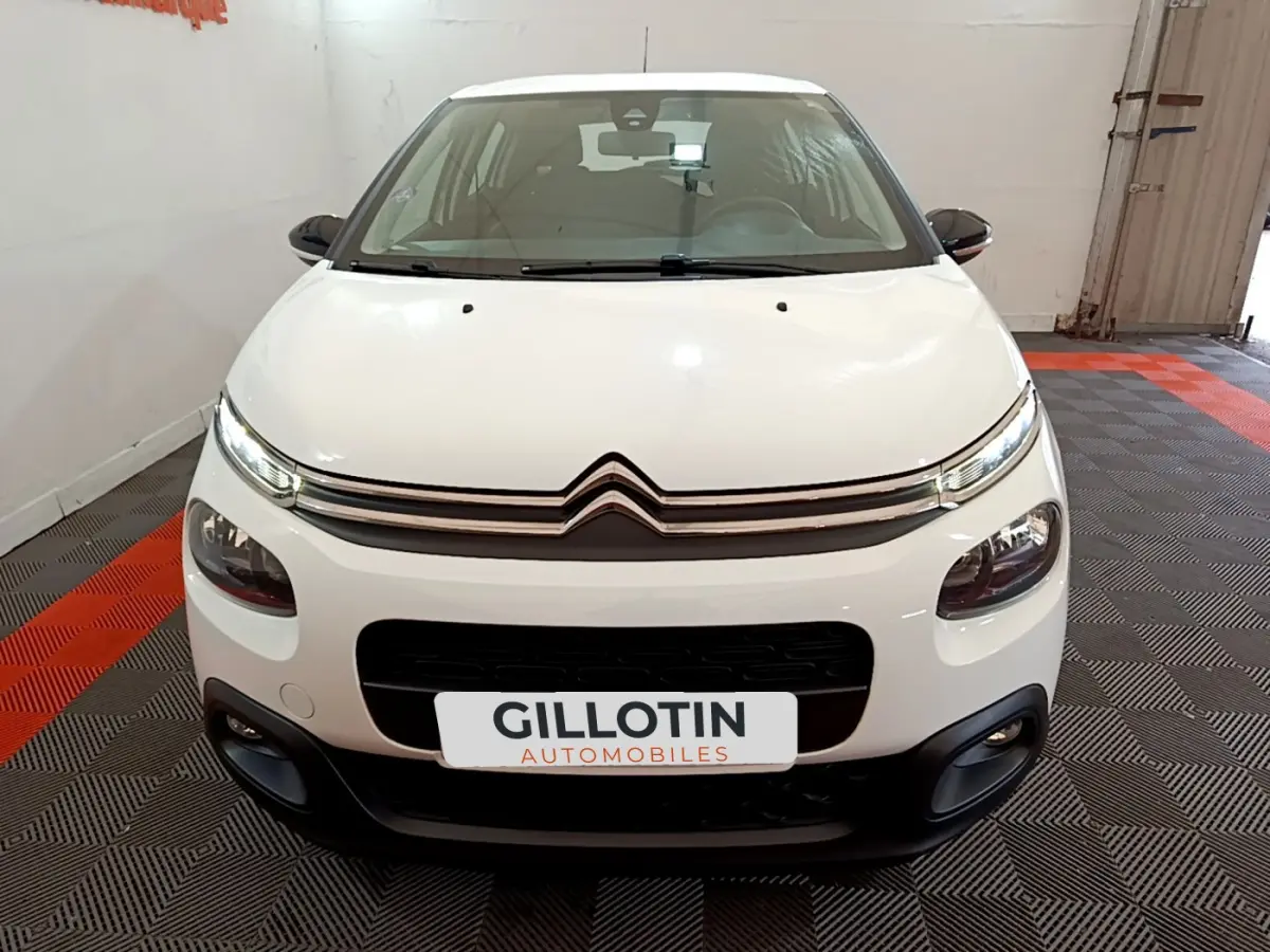Vue frontale d'une Citroën C3 blanche de 2018 avec phares LED et calandre chromée, en intérieur showroom.