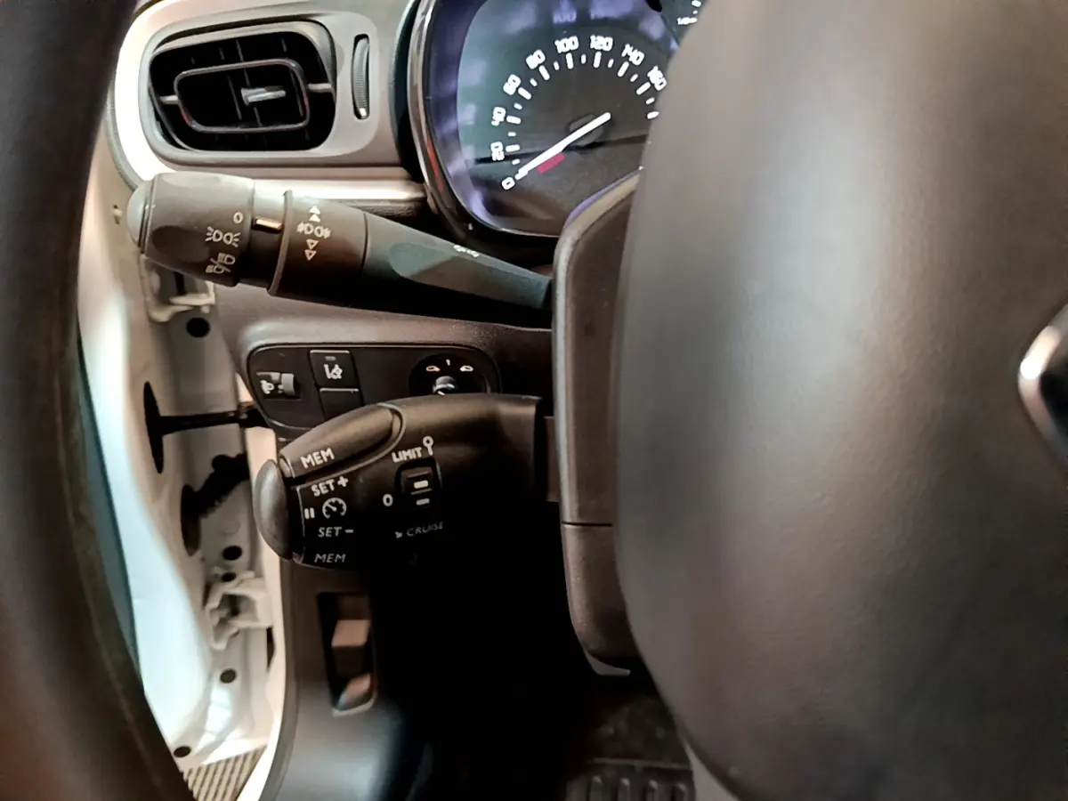 Gros plan sur le volant et les commandes de régulateur de vitesse d'une Citroën C3 blanche, côté gauche.