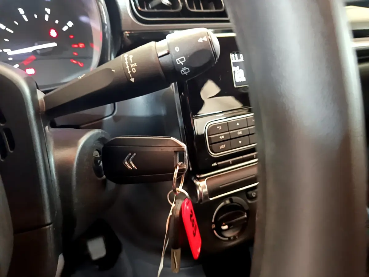 Gros plan intérieur sur le volant et la clé de contact avec logo Citroën, tableau de bord noir et commandes visibles.
