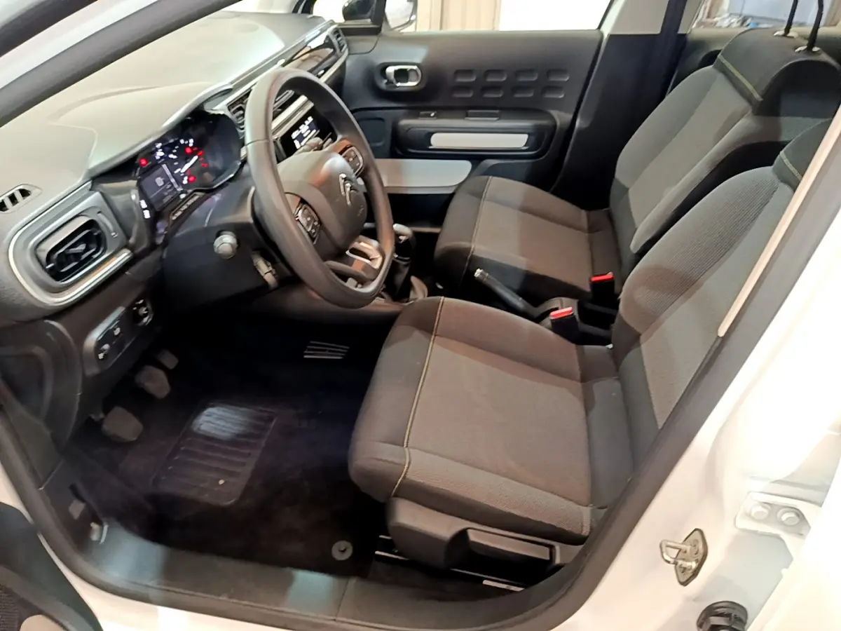 Intérieur avant droit d'une Citroën C3 blanche 2018, sièges tissu gris et tableau de bord avec volant multifonctions.