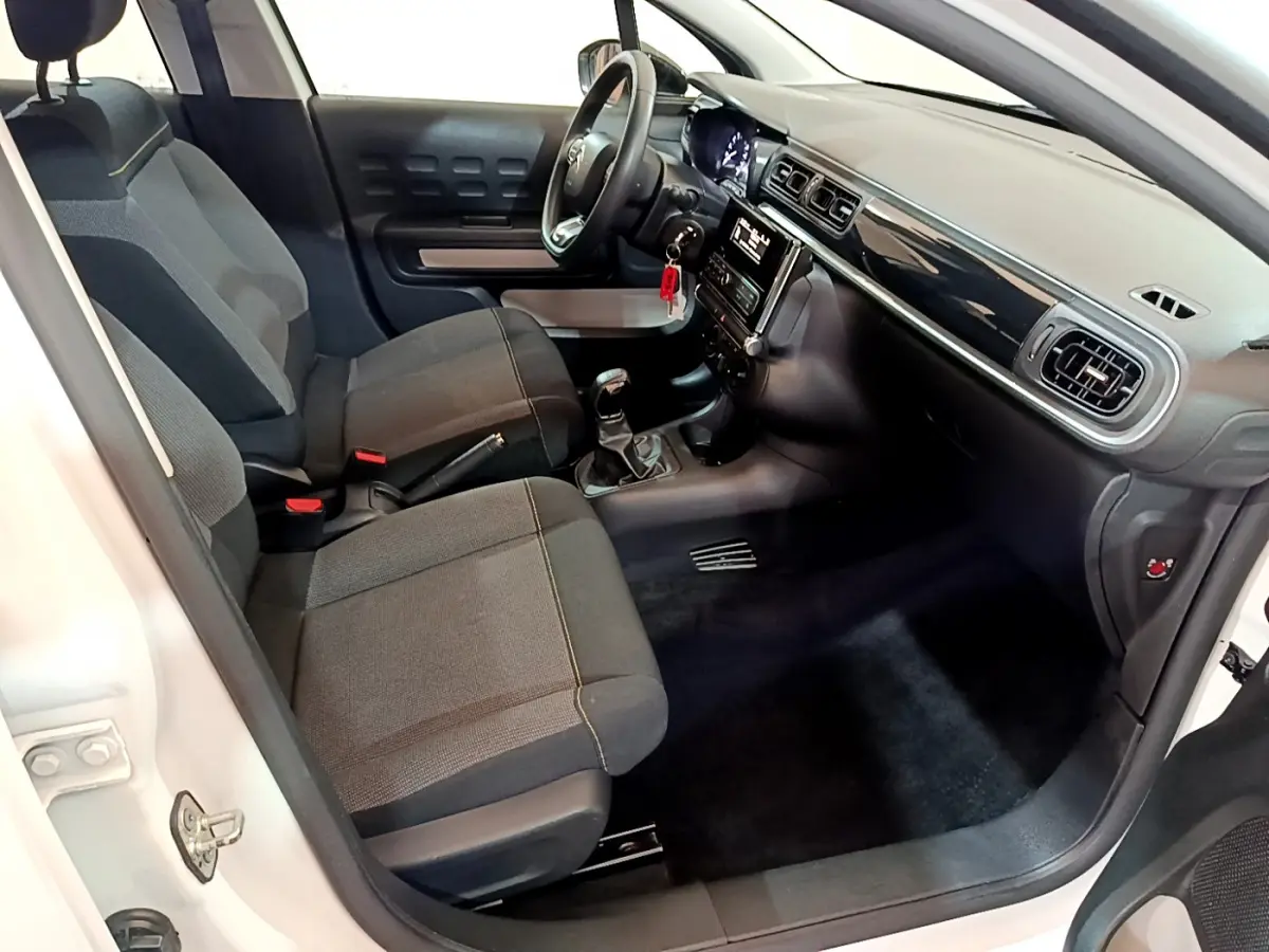 Intérieur avant droit d'une Citroën C3 blanche 2018, avec sièges tissu gris et tableau de bord noir brillant.