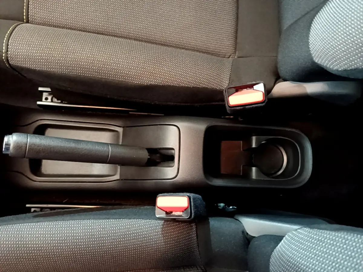 Vue plongeante sur la console centrale noire d'une Citroën C3 blanche, montrant frein à main et ceintures rouges.